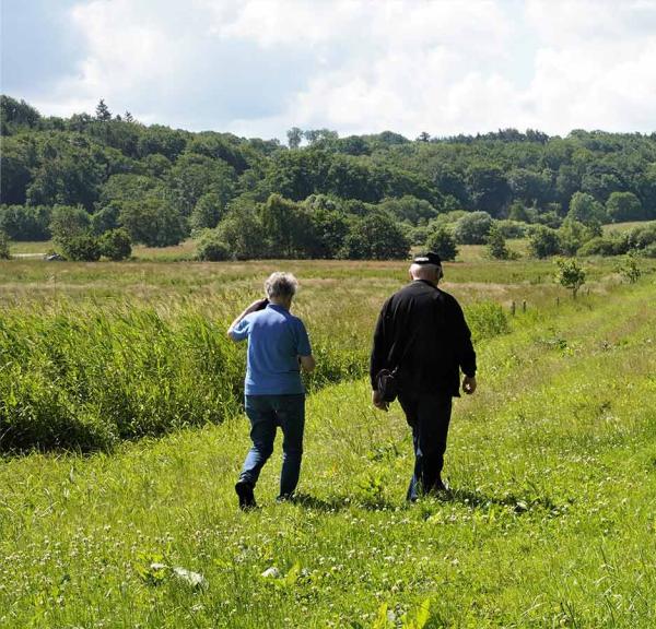 Two adults are walking in the sunshine on the green Ådal path at Ravningeboen.